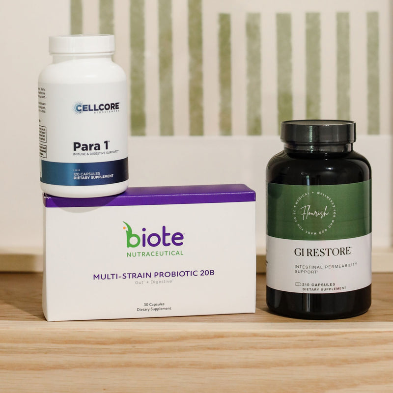 Three dietary supplement products arranged on a light wood surface: a white CELLCORE Para 1 bottle sitting on top of a white and purple biote box, next to a dark amber biote GIRESTORE bottle.