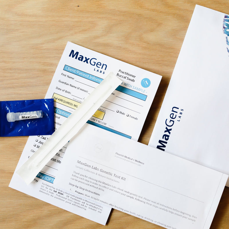 MaxGen Labs genetic test kit components arranged on a light wood surface, including printed forms, a white plastic pipette, a blue vial packet, and branded envelopes.