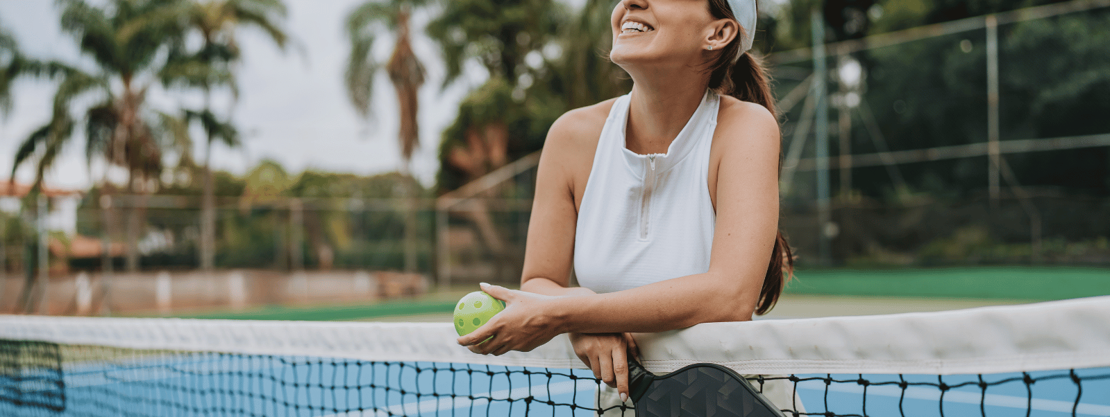 Woman holding a tennis ball on a tennis court with palm trees in the background