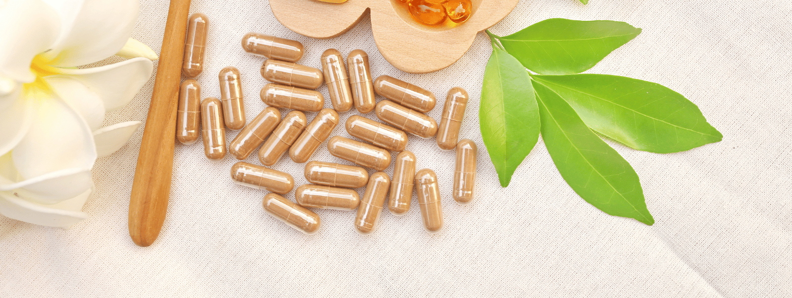 Gold capsules with a wooden stick and green leaves on a light background