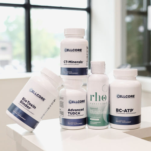 Five white supplement bottles from CellCore Nutrition arranged on a white surface in front of a softly blurred window background. The products include BioToxin Binder, CT-Minerals, Advanced TUDDCA, RhO Enzymed Glutathione, and BC-ATP.