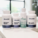 Four white supplement bottles from Cellcore Nutrition arranged on a white surface in front of a blurred window background. The bottles include BioToxin Binder, Advanced TUDCA, L-Theanine, and BC-ATP.