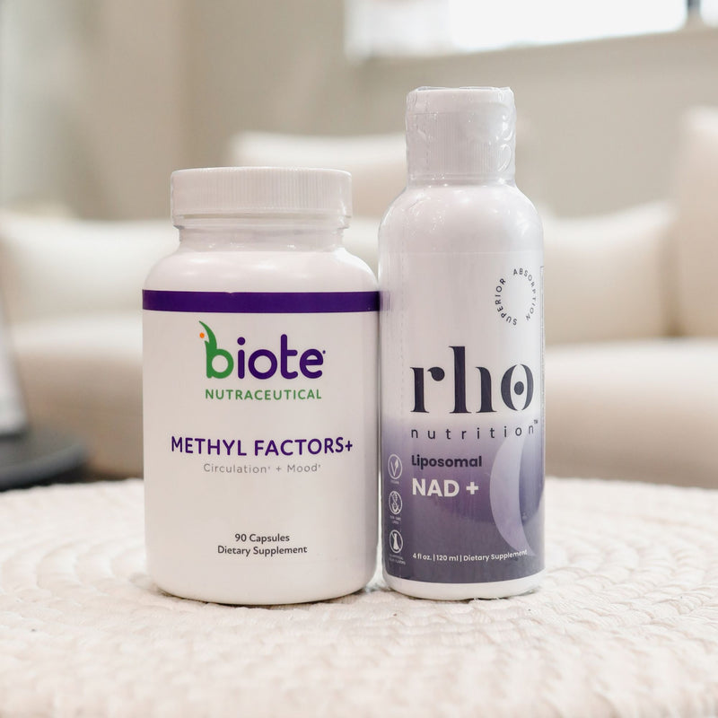 Two white supplement bottles standing side by side on a textured white surface in a softly blurred indoor setting. The left bottle is labeled biote Nutraceutical Methyl Factors+ and the right bottle is labeled rho nutrition Liposomal NAD+.