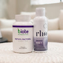 Two white supplement bottles standing side by side on a textured white surface in a softly blurred indoor setting. The left bottle is labeled biote Nutraceutical Methyl Factors+ and the right bottle is labeled rho nutrition Liposomal NAD+.