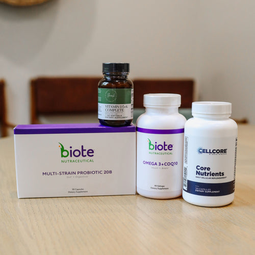 Three biote brand dietary supplement products arranged on a light wood tabletop: a white box labeled Multi-Strain Probiotic 208, a white bottle labeled Omega 3 + COQ10, and a white bottle labeled Core Nutrients, with a smaller dark bottle standing behind the box.