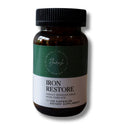 An amber glass bottle of Flourish Iron Restore dietary supplement with a black ribbed cap, featuring a green and white label, on a white background with a soft shadow.