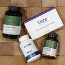 Four supplement products arranged on a brown cardboard background: a black bottle labeled GISTRESTORE, a white box labeled biote Nutraciential Multi-Strain Probiotic 208, a white bottle labeled Para 1, and an amber bottle labeled Digestiv 2 Enzymes. Two labels show the Harvestbridge logo.