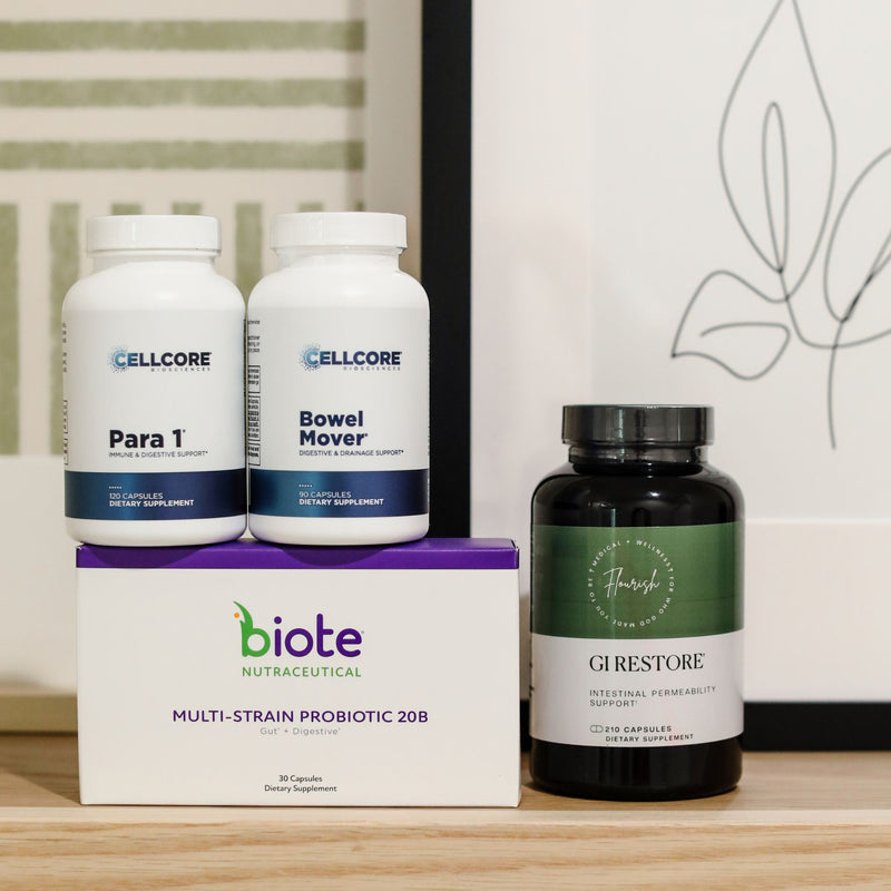 A group of dietary supplement products arranged on a light wood surface: two white bottles labeled CELLCORE Para 1 and Bowel Mover sit on top of a white biote box with purple accents, next to a black bottle labeled Gastrostore Gurestore Intestinal Permeability Support.