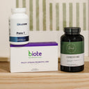 Three dietary supplement products arranged on a light wood surface: a white CELLCORE Para 1 bottle sitting on top of a white and purple biote box, next to a dark amber biote GIRESTORE bottle.