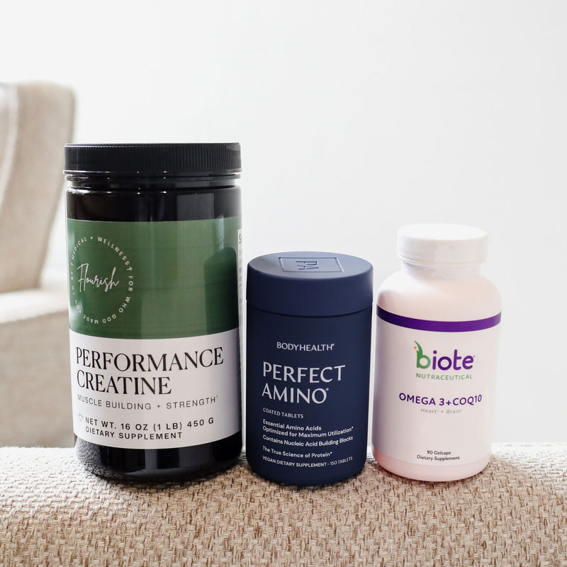 Three supplement containers arranged on a textured beige surface against a soft light gray background: a black jar labeled Flavour Performance Creatine, a navy blue canister labeled Bodyhealth Perfect Amino, and a pale pink bottle labeled biote Omega 3 + CoQ10.