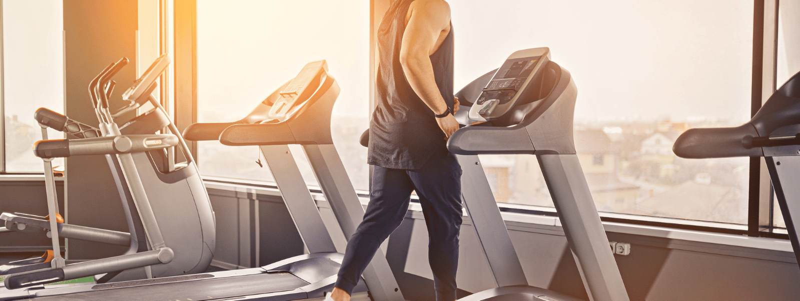 Person using a treadmill in a gym with large windows