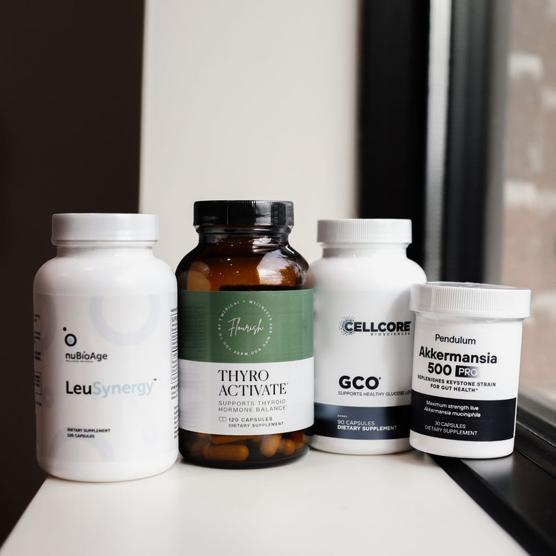 Four supplement bottles grouped together on a white windowsill: a white bottle labeled NuBioAge LeuSynergy, an amber bottle labeled ThyroActivate, a white bottle labeled CellCore GCO, and a white bottle labeled Pendulum Akkermansia 600 PC.