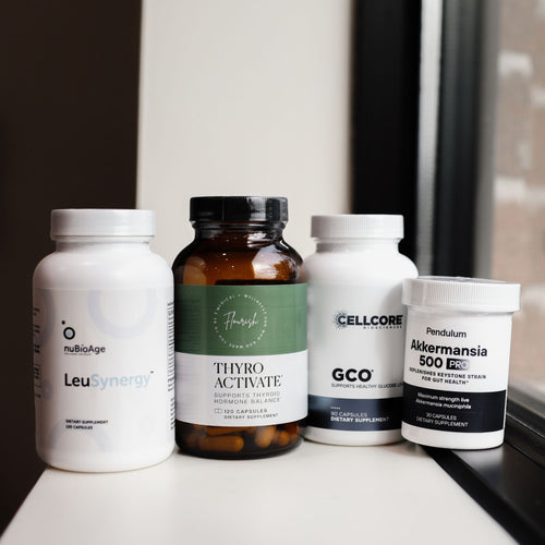 Four supplement bottles grouped together on a white windowsill: a white bottle labeled NuBioAge LeuSynergy, an amber bottle labeled ThyroActivate, a white bottle labeled CellCore GCO, and a white bottle labeled Pendulum Akkermansia 600 PC.